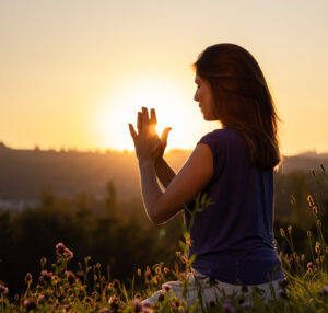 Nadine von naé yoga hat Hände in Gebetshaltung bei Sonnenuntergang auf einer Blumenwiese