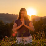 Nadine von naé yoga hat Hände in Gebetshaltung bei Sonnenuntergang auf einer Blumenwiese