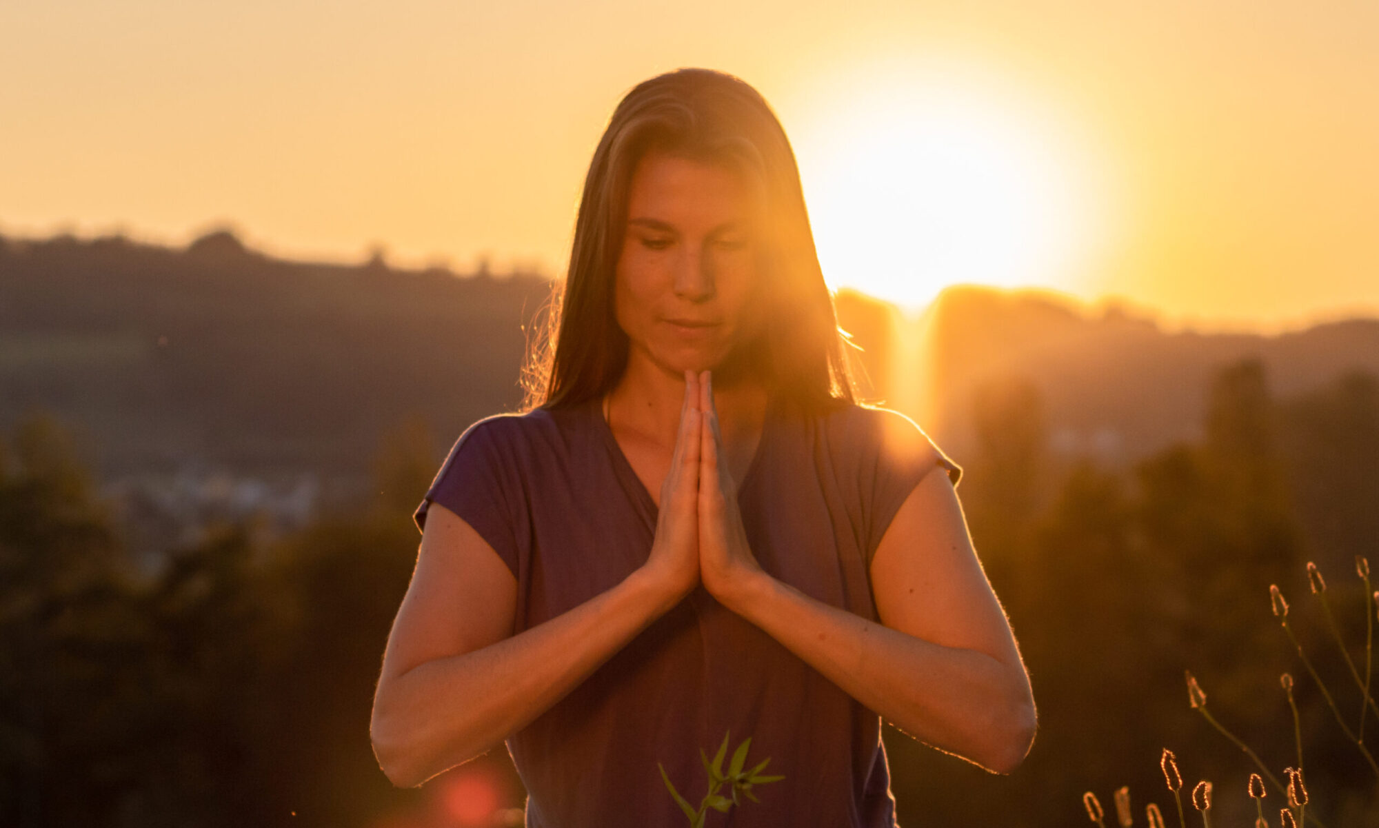 Nadine von naé yoga hat Hände in Gebetshaltung bei Sonnenuntergang auf einer Blumenwiese
