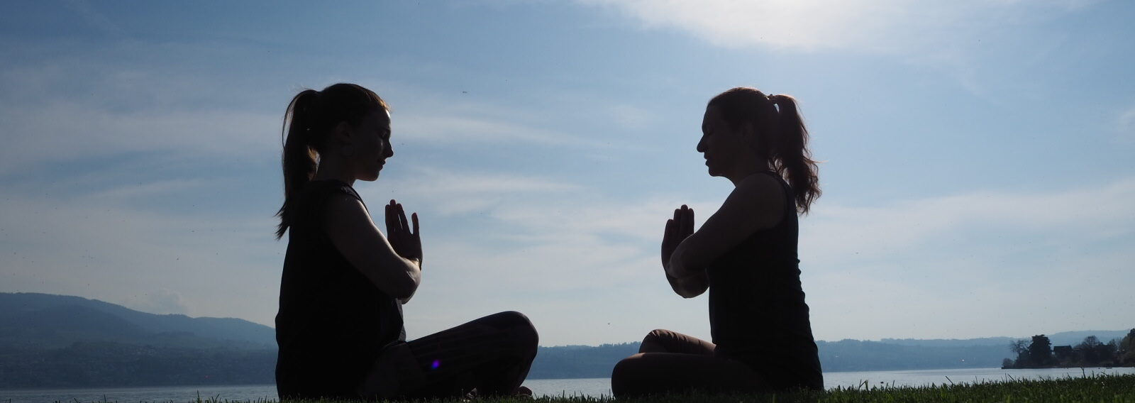 Nadine von naé yoga mit Chantal von Tada Yoga machen die Yoga-Pose Sukhasana am See in Uerikon