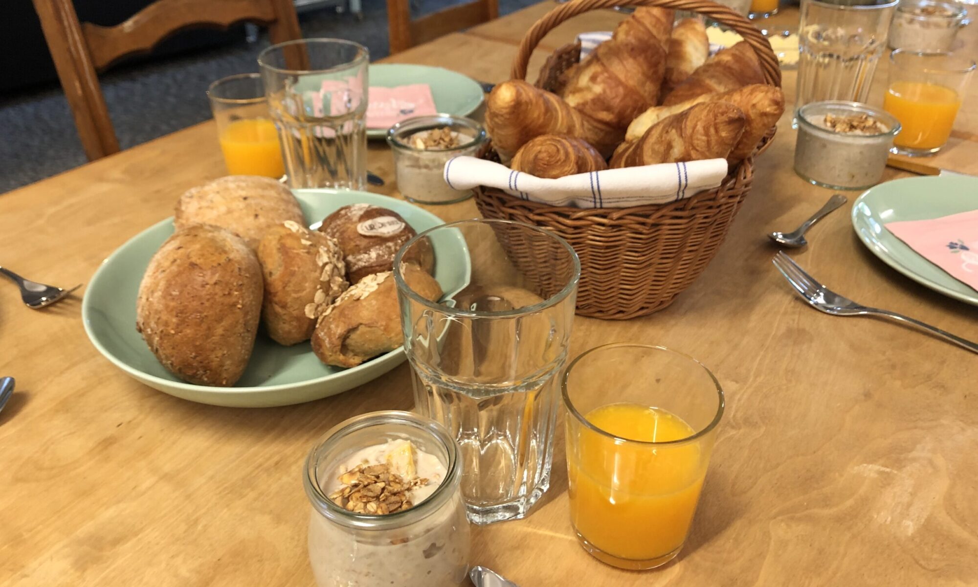 Croissants, Brötchen und Birchermüsli auf einem Holztisch